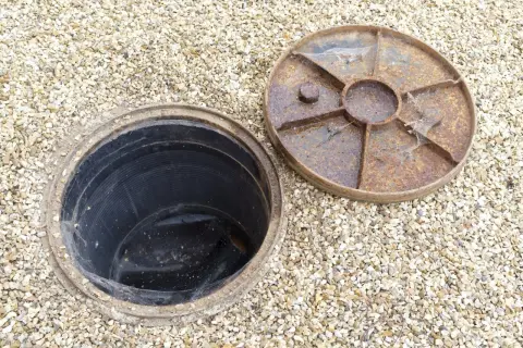 Un regard sur une canalisation d'eau pluviale ouverte, prête à être débouchée. Le couvercle rouillé est à côté.
