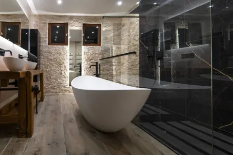 Salle de bain moderne avec baignoire îlot blanche et douche à l'italienne aux murs de marbre noir.