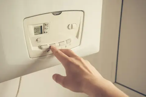 Main d'une personne appuyant sur les boutons d'une pompe à chaleur. Faut-il éteindre sa pompe à chaleur l'été ?
