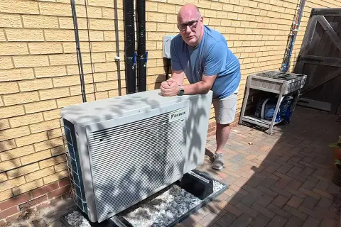 Un homme pose près d'une unité extérieure de pompe à chaleur Daikin, un système efficace pour le chauffage et la climatisation, potentiellement alimenté par une énergie solaire.