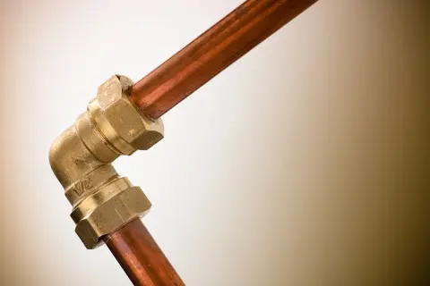 Un coude en laiton relie deux tuyaux en cuivre. Ce raccord per cuivre assure une connexion solide pour la plomberie.