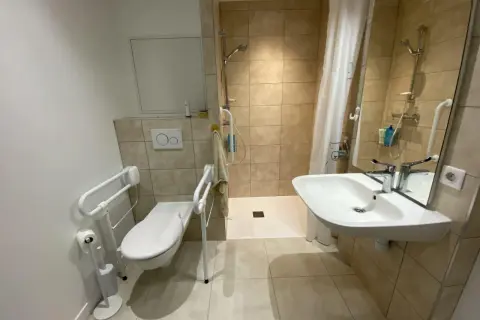 Salle de douche pmr avec WC adapté, barre d'appui, lavabo et douche à l'italienne. Confort et sécurité assurés.