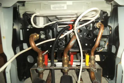 Vue intérieure d'une chaudière Saunier Duval, montrant les tuyaux en cuivre et les vannes. Vérification de la pression chaudière Saunier Duval.
