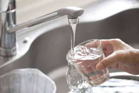 Main d'une personne remplissant un verre d'eau du robinet à Paris. L'eau claire coule du robinet chromé dans le verre.