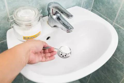 Une main verse du bicarbonate de soude dans un évier, une méthode naturelle pour le déboucheur canalisation maison.