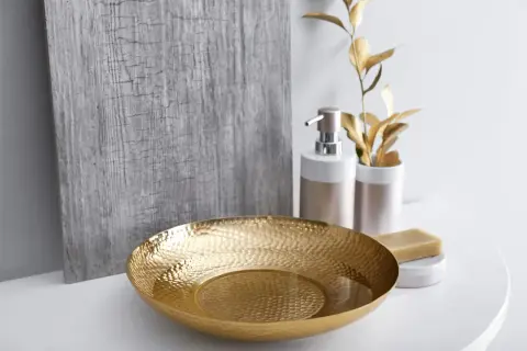Un bol texturé doré, un distributeur de savon et une barre de savon sur un comptoir blanc, évoquant une ambiance de douche dorée.