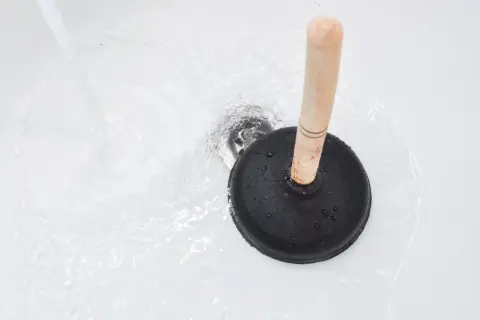 Ventouse sur un drain de baignoire avec de l'eau qui coule. Une solution simple pour savoir comment déboucher une baignoire rapidement.