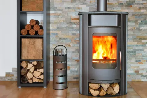 Un poêle à bois crépitant, avec du bois rangé à côté. Un accessoire pour le feu est présent.
