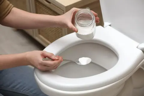 Une personne utilise une cuillère de bicarbonate de soude comme déboucheur canalisation maison pour un WC.