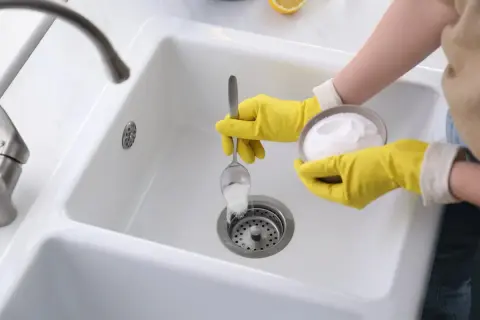 Main jaune versant du percarbonate dans un évier blanc pour le déboucher. Solution écologique et efficace.