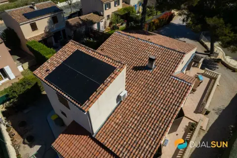 Toits de maisons avec panneaux solaires noirs. Une unité extérieure de pompe à chaleur est visible sur le mur.