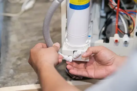 Mains d'un technicien connectant un tuyau à un appareil. Mon adoucisseur ne consomme plus de sel, il est temps de vérifier les connexions.