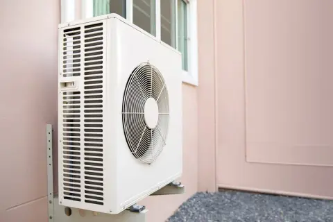 Unité extérieure d'une pompe à chaleur, installée sur un mur rose. Le ventilateur est visible, prêt à assurer le confort thermique.