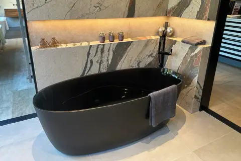 Baignoire noire en acrylique, prête pour un nettoyage. Un drap de bain gris est accroché.