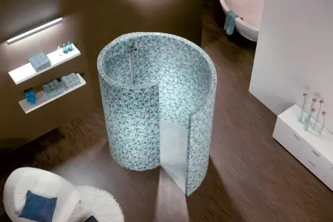 Une douche escargot aux mosaïques bleues et vertes, avec une baignoire et un fauteuil blanc dans une salle de bain moderne.