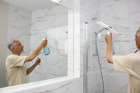 Un homme nettoie la porte de douche en verre pour enlever le calcaire.