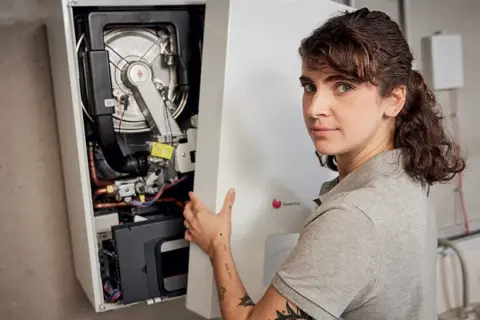 Une technicienne installe une chaudière F28. Elle tient le panneau avant ouvert, révélant les composants internes.