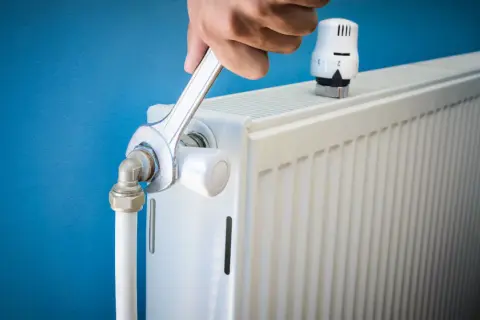 Réparation d'un radiateur bruyant. Une clé serre un raccord, peut-être pour arrêter l'eau qui coule.